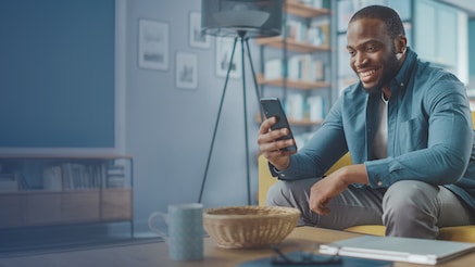 Smiling man sitting on living room couch looking at his smartphone
