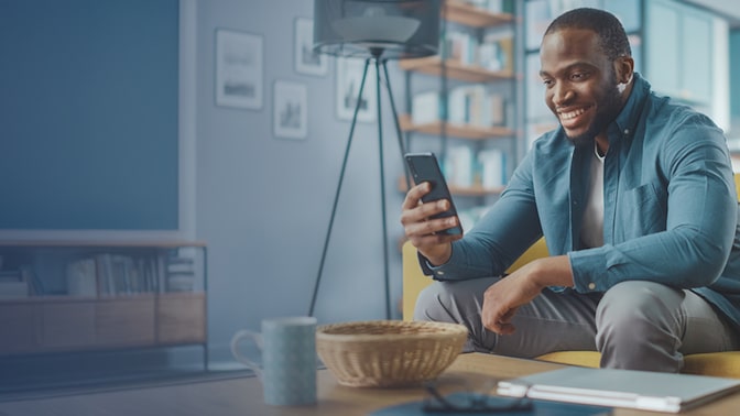 Smiling man sitting on living room couch looking at his smartphone