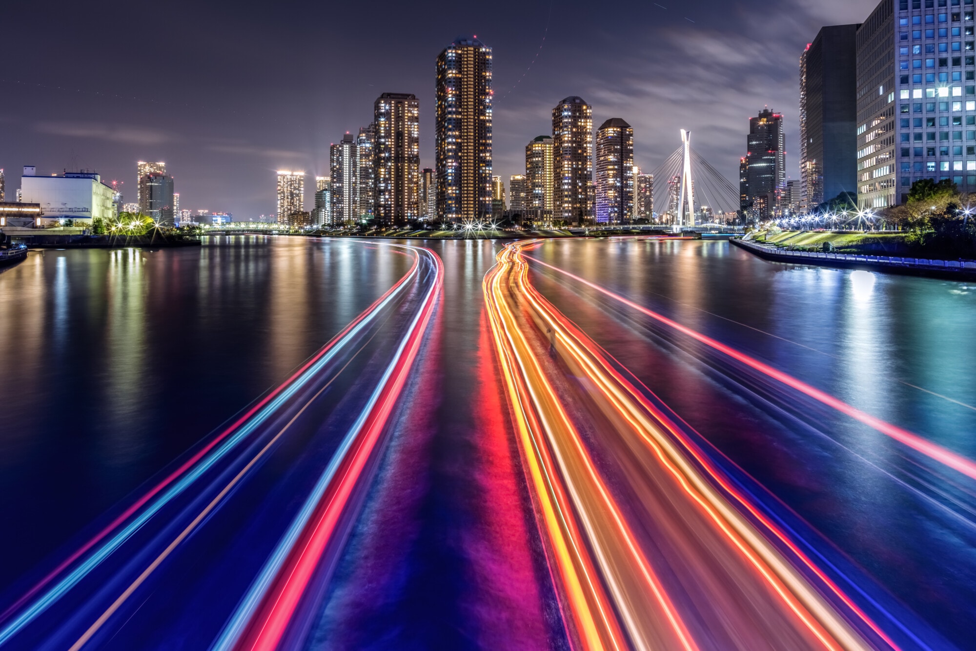 Night skyline with illuminated skyscrapers and colorful light trails on river in modern city waterfront.