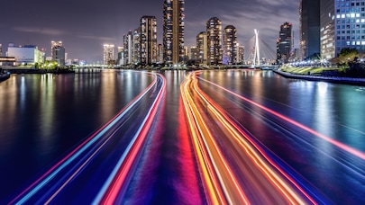 Night skyline with illuminated skyscrapers and colorful light trails on river in modern city waterfront.