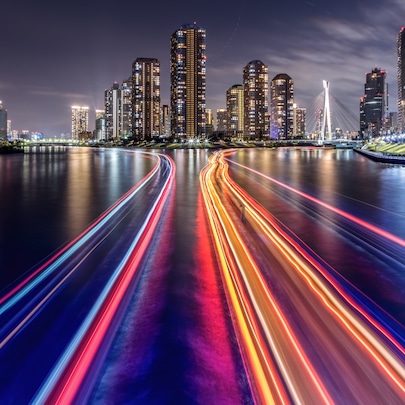 Night skyline with illuminated skyscrapers and colorful light trails on river in modern city waterfront.