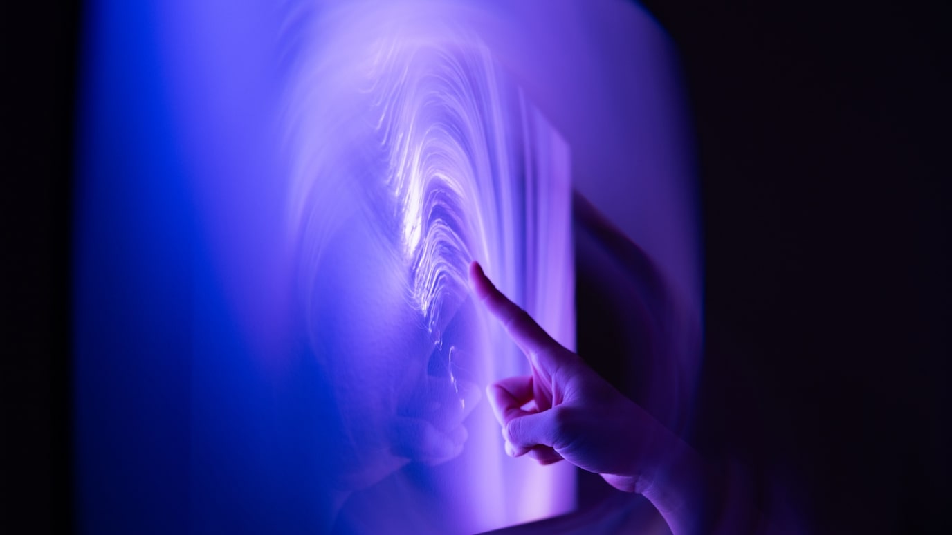 Hand touching glowing digital wave pattern on screen in blue and purple light.