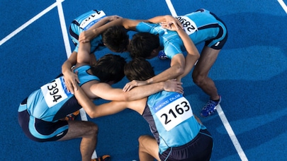 Four relay runners huddle on blue track preparing for race start