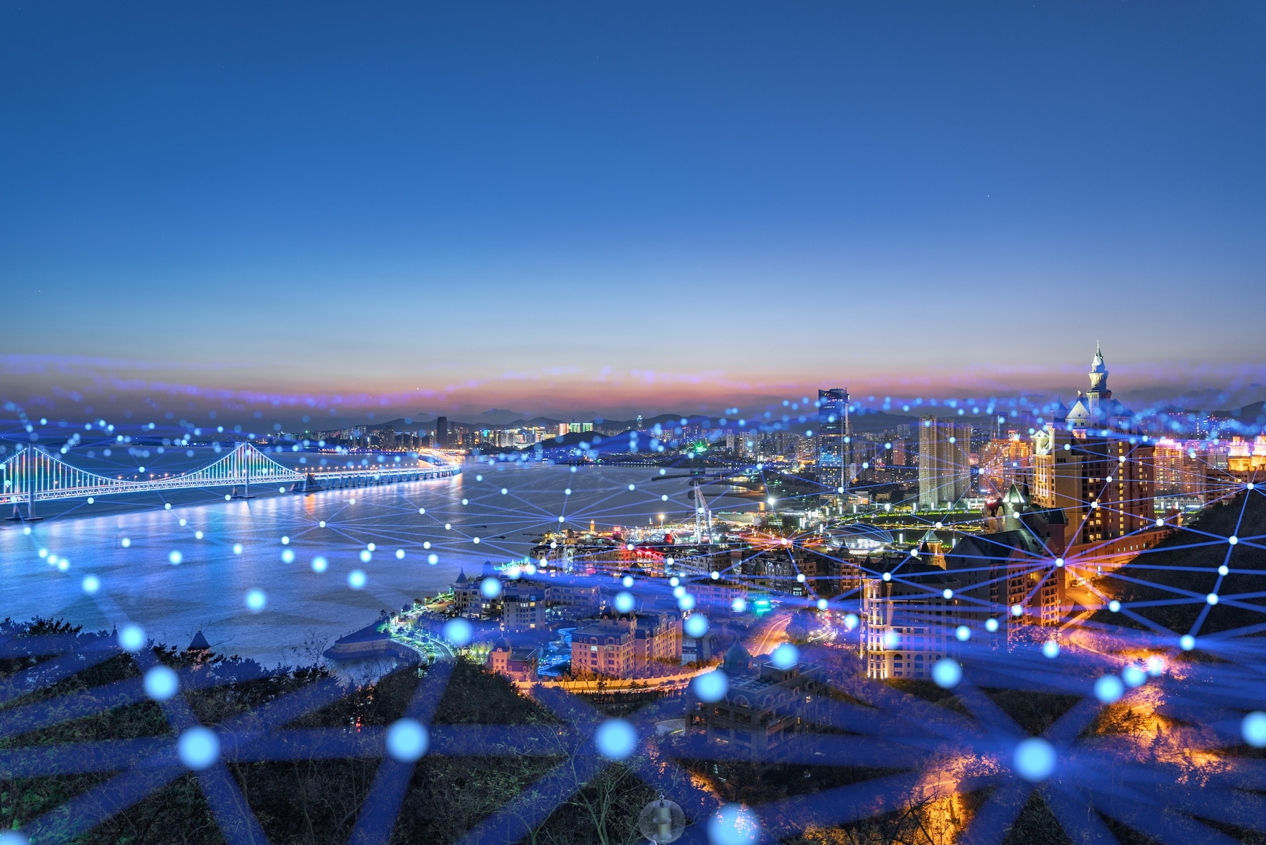 Night city skyline with illuminated bridge and waterfront, overlaid with glowing digital network connections across urban landscape