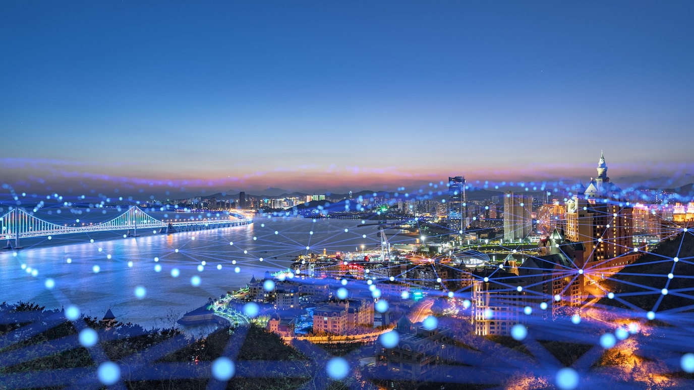 Night city skyline with illuminated bridge and waterfront, overlaid with glowing digital network connections across urban landscape