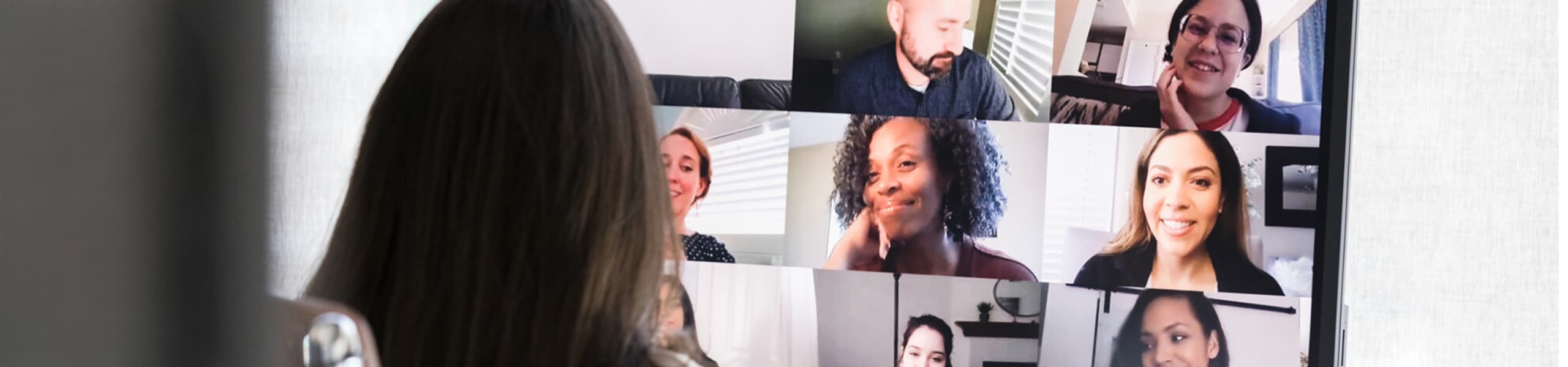 Woman participating in online meeting with meeting participants on monitor in front of her