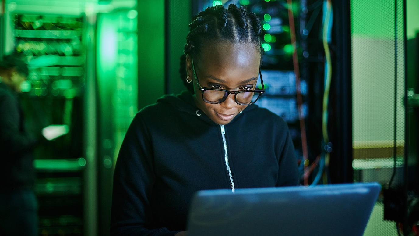 Woman bathed in green light while on laptop in server room