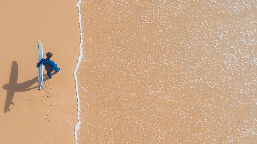 Overhead view of surfer carrying surfboard as he walks along the beach