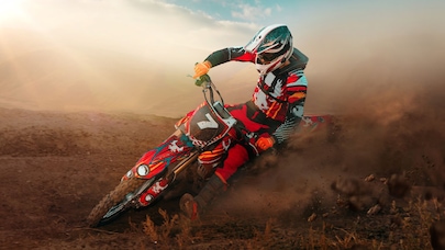 Motocross rider carving through dirt trail, kicking up dust at high speed outdoors