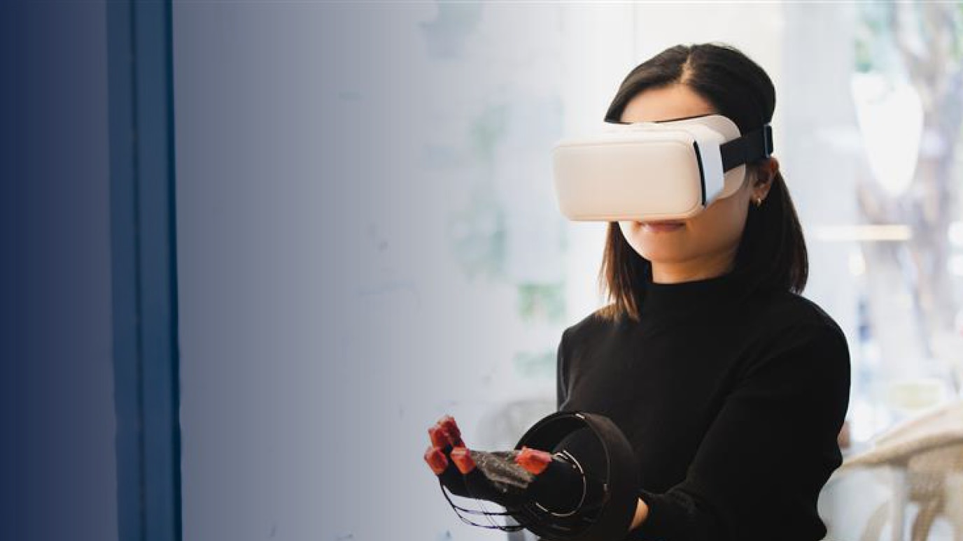 Woman wearing VR headset and haptic glove interacting with virtual environment indoors in lab rooms