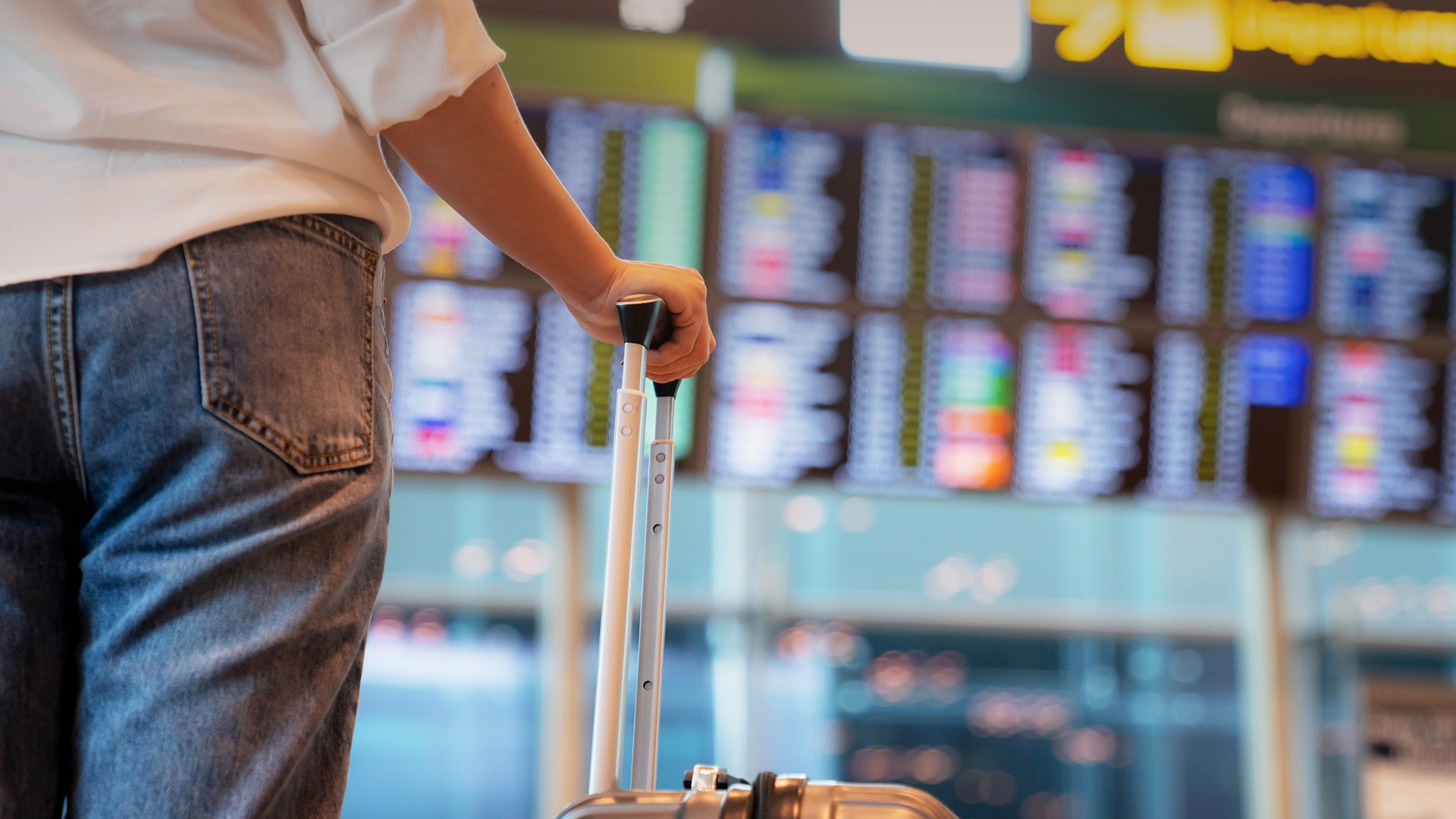 Traveller with suitcase standing in front of departures board
