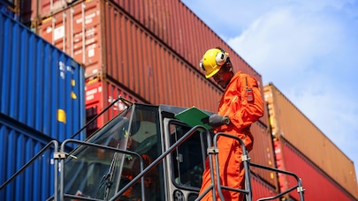 Man in hardhat checking info on clipboard in front of shipping containers