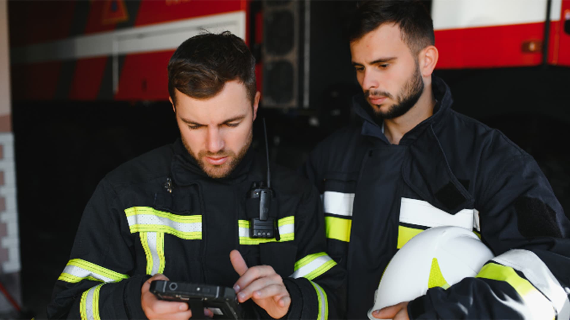 Two firemen looking at tablet device in front of fire engine parked inside a fire station