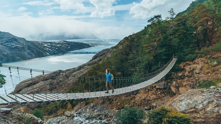 Woamn crossing rope bridge on hill overlooking river
