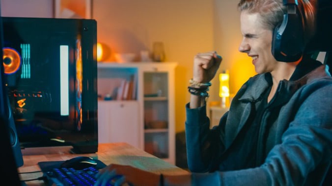 Woman wearing headphones facing monitor, fist raised in celebration  