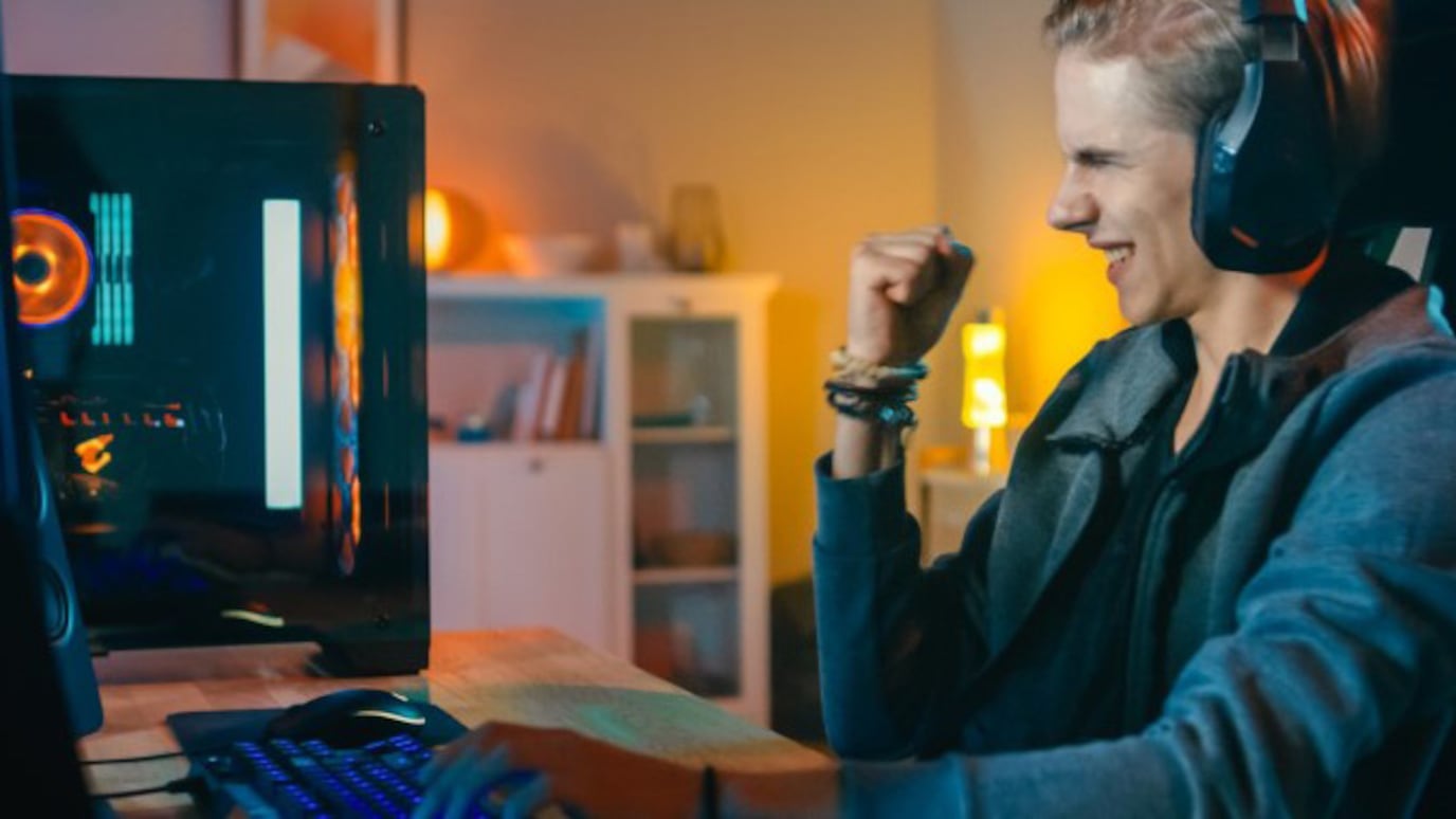 Woman wearing headphones facing monitor, fist raised in celebration  