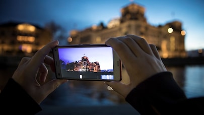 A person photographing a historic waterfront building with a smartphone at dusk.