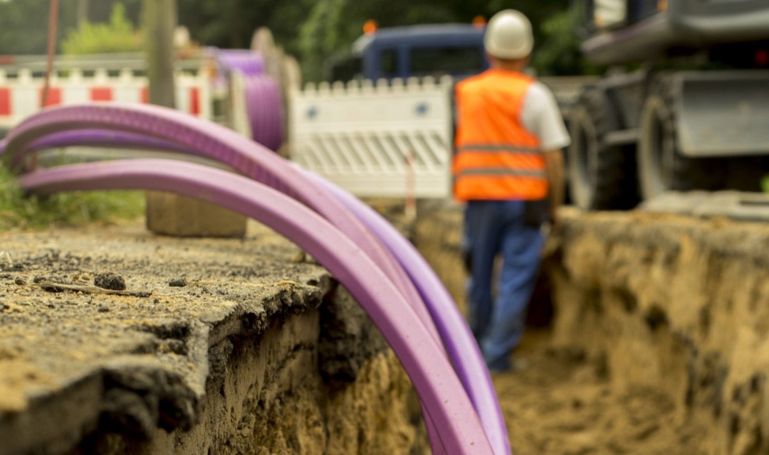 Engineer standing in construction trench with coil of fiber optic cable in foreground