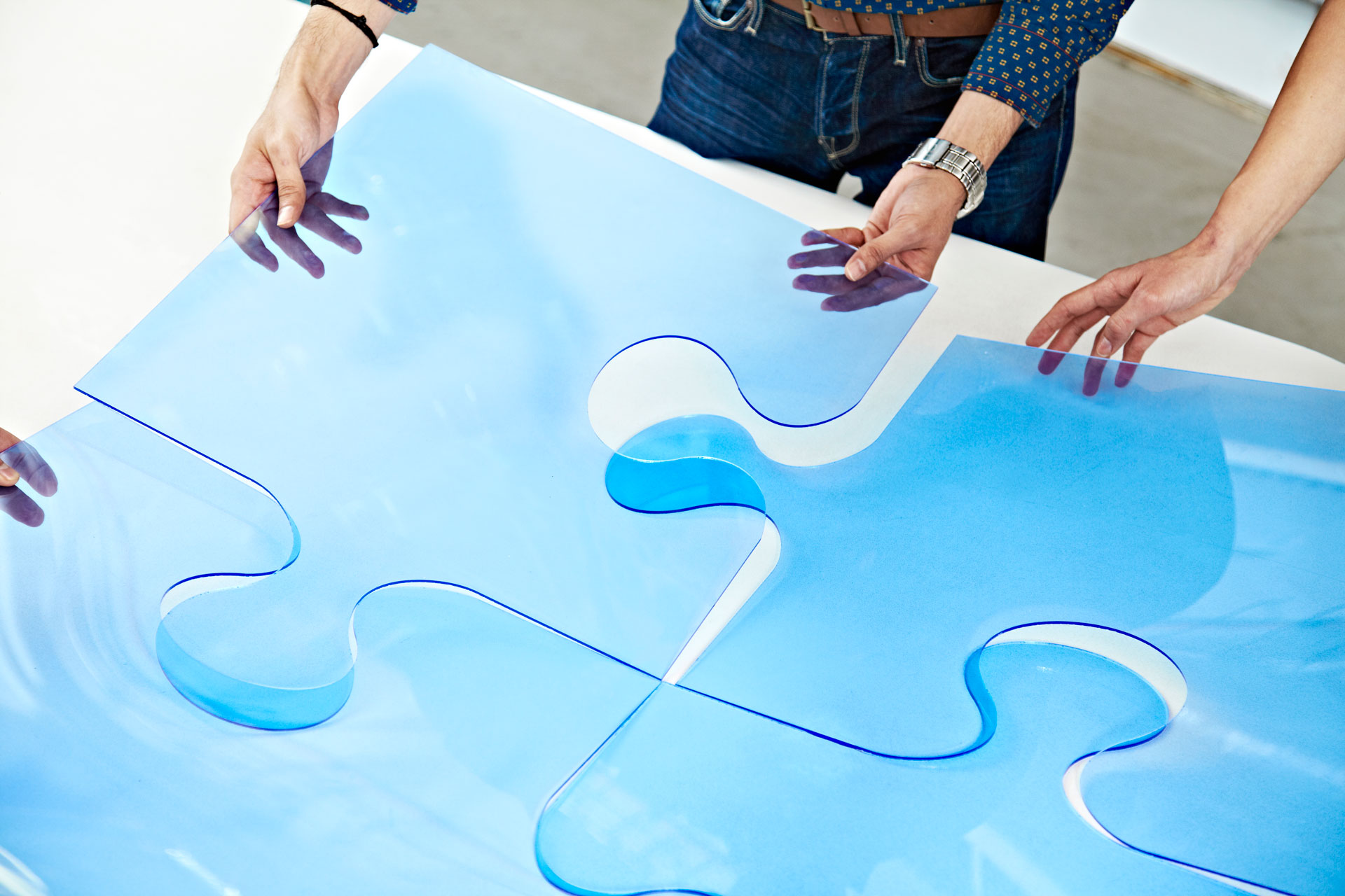 Multiple hands assembling a large blue jigsaw puzzle, symbolizing teamwork and problem-solving.