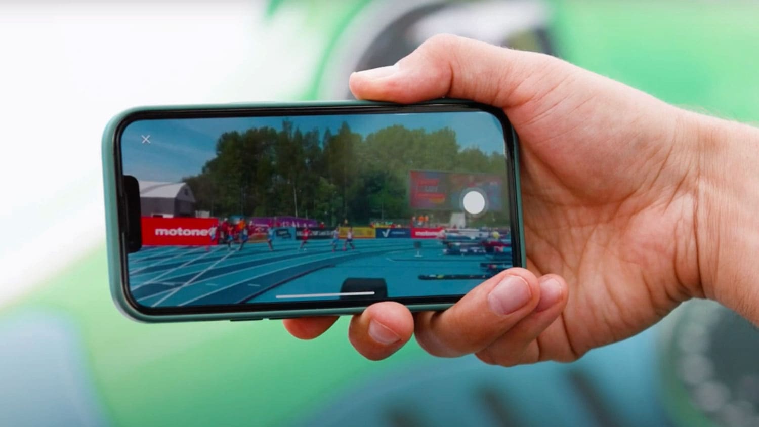 A person holding a smartphone, watching a live sporting event on the screen.