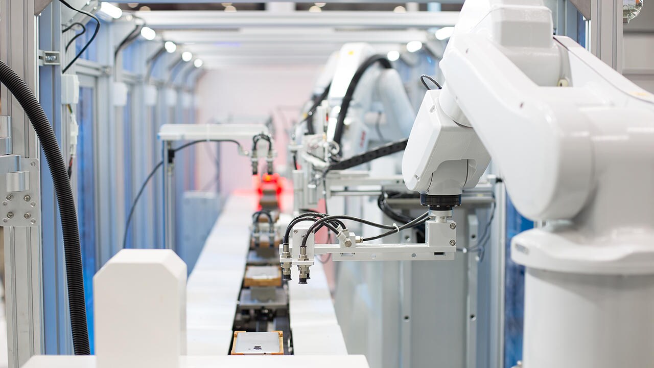 A modern manufacturing assembly line featuring robotic arms equipped with precision tools, operating on a conveyor belt with organized components.