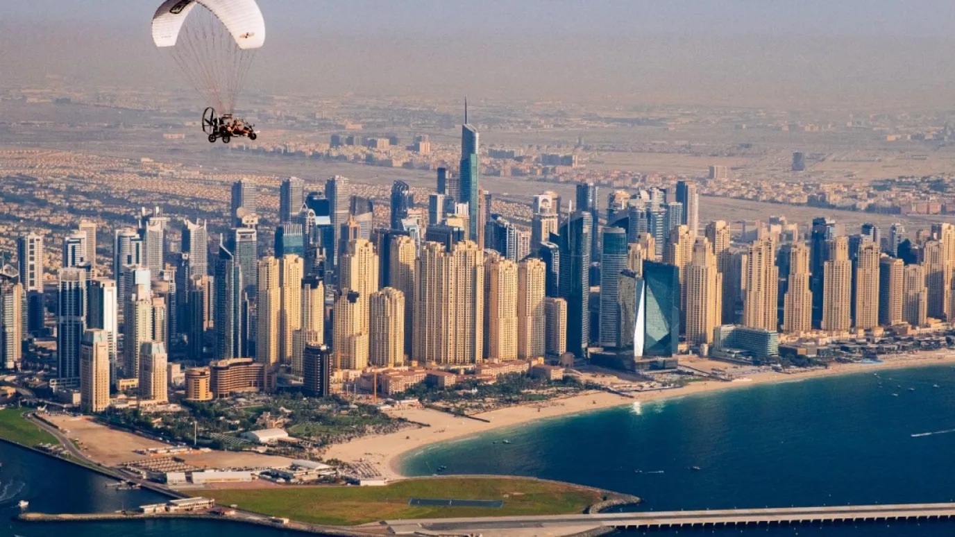 Photograph of microlite flying towards city with skyscrapers