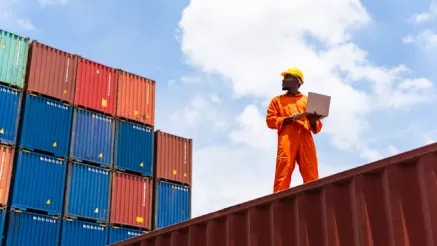 A person wearing safety gear standing among containers.