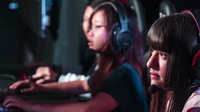 Three young people sitting by gaming PCs wearing headsets.