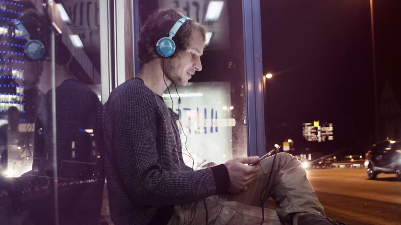 A person sitting at a bus stop at nighttime with their headphones on.