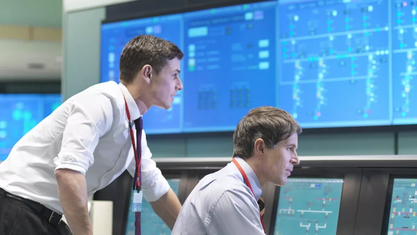 Two men working by the same computer screen.