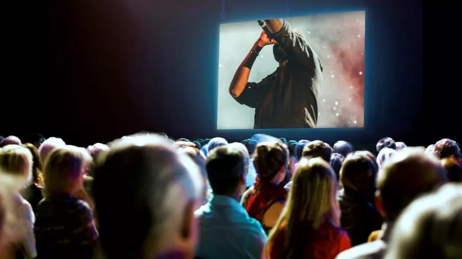 A crowd of people watching a live music performance from a large screen.