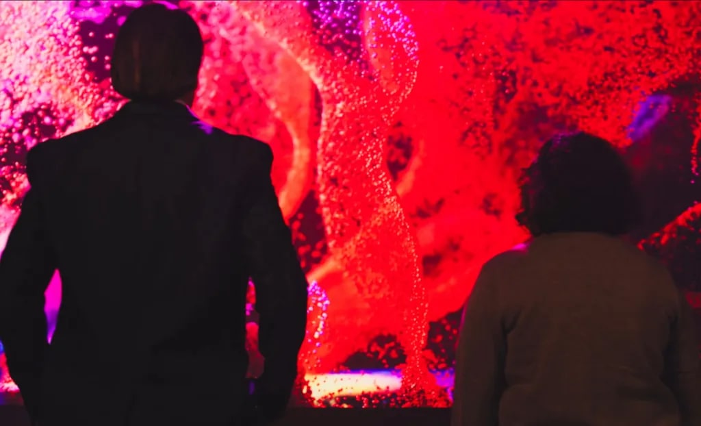 Man and woman looking into a large LCD screen showing a vivid swirling neon bubble vortex