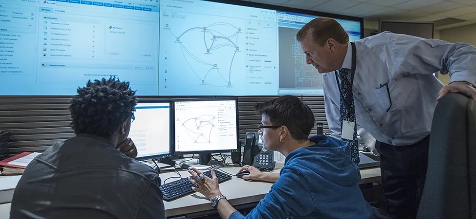 Three people looking at monitors in a command center