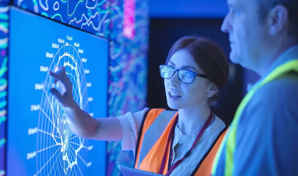 One engineer explaining a topic to another using a large touch-screen display