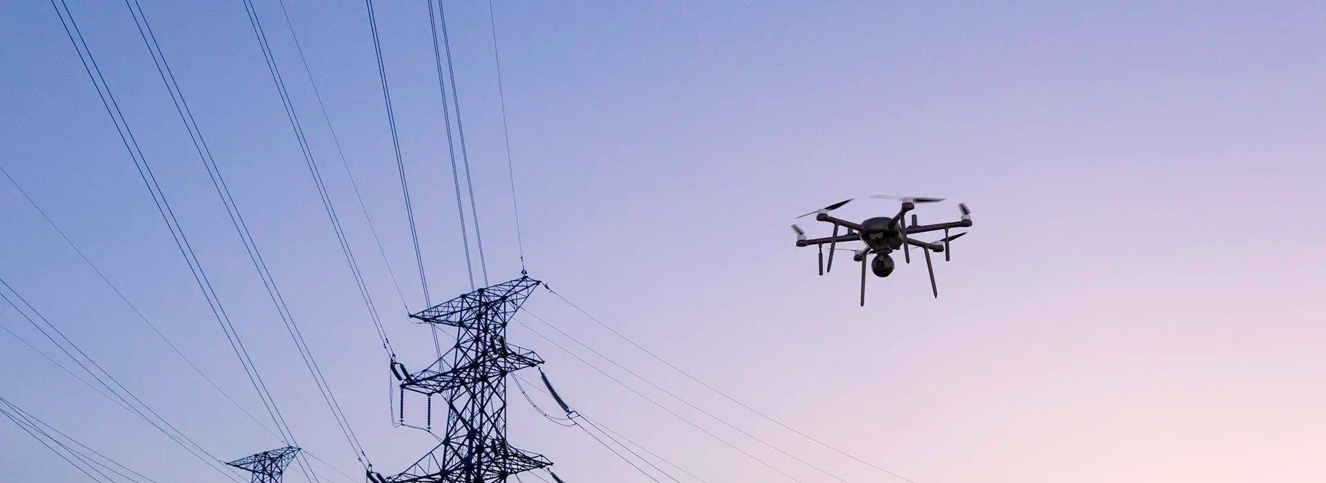 An image showing a drone flying next to power lines at dusk.