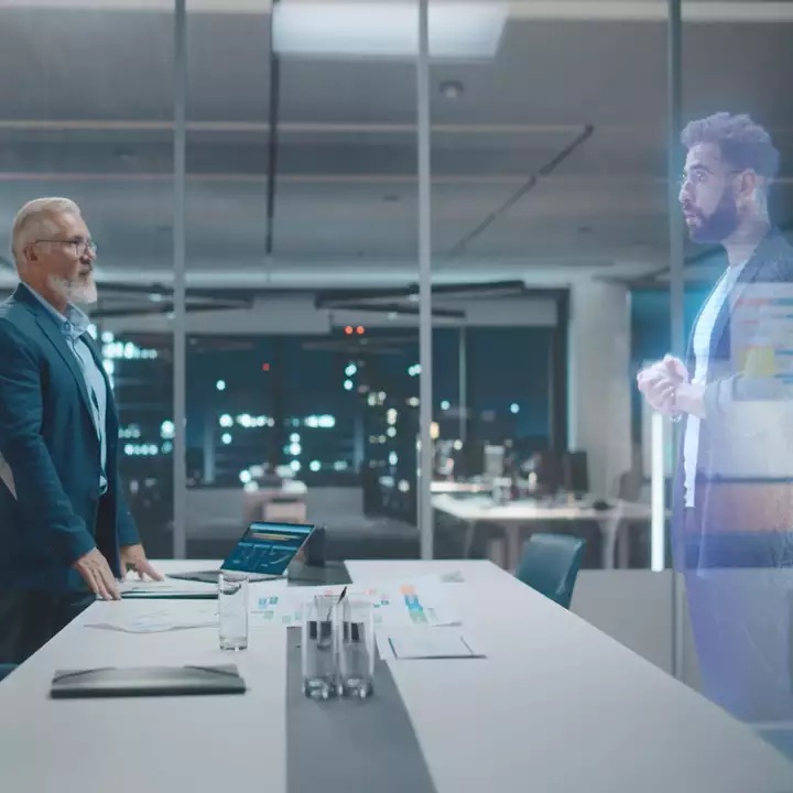 A business person conversing with a hologram of another person in a boardroom