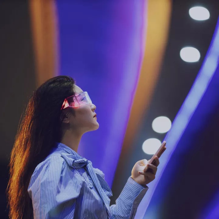 Woman wearing smartglasses amd holding smart phone looking up at lights